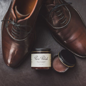 Brown Water Resistant Leather Cream jar opened next to a pair of brown leather oxfords and a jar of Leather Cleaner and Conditioner.