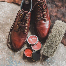 Load image into Gallery viewer, Burgundy Water Resistant Leather Cream jar open next to a Burgundy Shoe Polish Wax tin, all beside a pair of burgundy lace-up boots and a horsehair brush.