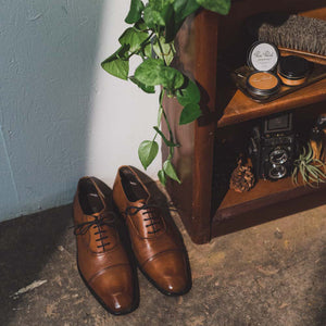 Pair of leather cap-toe oxfords next to a shelf with light brown leather cream polish and shoe polish paste/wax