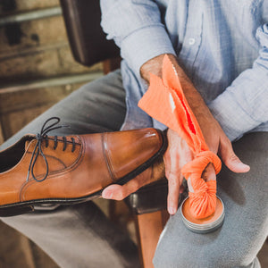 Orange High Quality Shoe Polishing Cloth wrapped around man's fingers as he dabs into a tin of shoe polish wax
