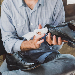 Man polishing a pair of black leather wingtip derby shoes with a premium cotton shoe polishing cloth