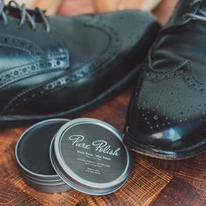 Black Paste/Wax Tin open next to a pair of black brogue wingtip leather shoes