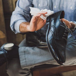 Man applying high shine shoe polish wax to the heels of his black leather dress wingtips