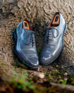 Pair of Grey Allen Edmonds Park Avenue cap-toe dress shoes polished against a tree 