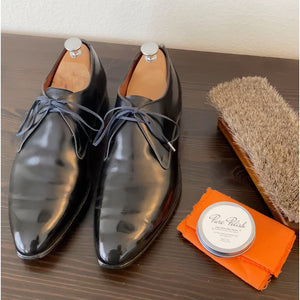 Mirror shined pair of black derby shoes next to a tin of Pure Polish High Shine Shoe Polish Wax