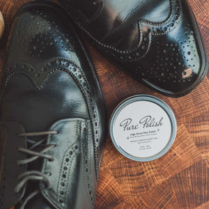 Tin of Pure Polish High Shine Shoe Polish Wax next to a pair of shined black leather brogues