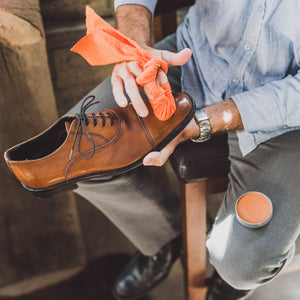 Man polishing the toes of a pair of light brown cap-toe oxford shoes with a tin of Light Brown Shoe Polish Paste / Wax by Pure Polish